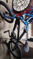 Side view of black Mongoose BMX bike with blue detail and hand brakes, leaning vertically against a wall.