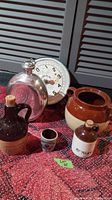 Lot showing a vintage hanging scale, silver-colored canteen, large two-tone brown/beige bean pot, and two stoneware jugs with cork stoppers.