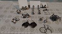 Overview of 11 pairs of silver pierced earrings of various styles laid out on lace tablecloth.