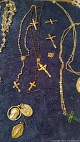Overview of religious pendants on a blue towel including several cross necklaces, religious medals, and a butterfly pendant.