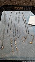 Five silver chains and four pairs of pierced earrings including two dangling pairs and one pearl stud pair, displayed on a soft fabric.