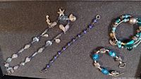 Full view of all four jewelry pieces on dark surface showing bracelets and necklaces with blue beads and silver charms