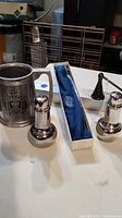 Photo of a pewter mug with insignia, two sterling silver salt and pepper shakers, and a sterling silver candle snuffer in a blue velvet-lined box.