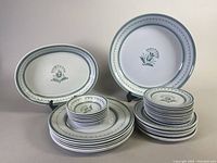 Full set of 1960's Arabia Finland Green Thistle dishes stacked and displayed, showing different plate sizes and bowls with hand painted design.
