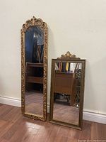 Both mirrors placed on hardwood floor showing overall size difference and portraits