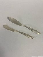 Two Wallace sterling silver spreader knives on a plain surface, showing full length and shape