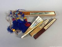 Four Asian handheld folding fans displayed folded alongside a wooden box.