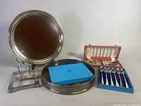 Photo showing silver plated serving tray on stand, round serving tray, boxed sets of utensils and spoons.