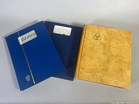 Three stamp albums side by side showing blue 'GERMANY' labeled, blue cursive labeled 'Germany', and beige triple circle logo album
