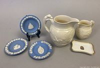 Three Wedgwood blue jasperware plates with classical white relief motifs, two white relief Wedgwood pitcher and creamer, and a small Coalport Egyptian pharaoh trinket dish with gold trim