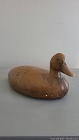 Front angled view of brown plaster duck figurine exhibiting surface wear and chips.