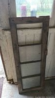 Old rectangular wooden window frame with four clear glass panels separated by wooden muntins, showing age and wear.