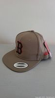 Front and left side view of the brown snapback hat with Boston Red Sox logo and New Era branding.