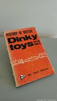 Front cover of the book 'History of British Dinky Toys 1934-1964' by Cecil Gibson showing title, author, and vintage vehicle illustrations on an orange background.