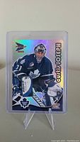 Front side of Curtis Joseph hockey trading card with holographic finish showing him in goalie gear in action pose. Card is in plastic holder on a stand.