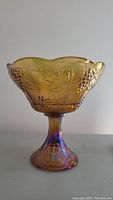 Front view of Indiana Glass iridescent marigold carnival glass compote showing scalloped edge and grape/leaf pattern.
