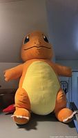 Front view of large Charmander stuffed plush showing orange body and yellow belly with detailed facial features.