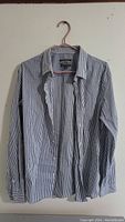 Front view of the striped men's dress shirt hanging on hanger, showing collar, buttons, and long sleeves.