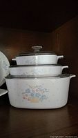 Three stacked white CorningWare casseroles with Blue Ribbon Flower Basket pattern and their glass lids