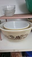 Two vintage Pyrex nesting mixing bowls stacked together, showing the cream color and brown floral swirl design on the larger bowl.