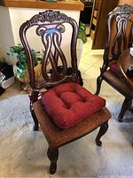 Front view of one wood carved dining chair with detailed carvings and red cushion on seat.