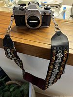 Front view of the Canon AE-1 camera body with colorful patterned strap hanging over a ledge.