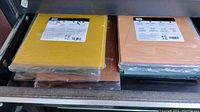 Close-up photo of stacks of colored cardstock paper, including yellow and peach sheets, packaged in plastic and placed in a drawer