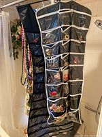 Two black hanging organizers with clear labeled pockets filled with various costume jewelry pieces including earrings, bracelets, necklaces, pins, and misc items
