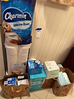 Photo showing Charmin Ultra Soft Family Mega toilet paper pack, wound care kits, and Tubigrip bandage boxes stacked against a wall.