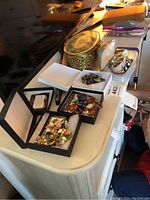 Wide shot of jewelry lot items including beaded necklaces, watches, a bracelet, a trinket box, and brooches laid out on a cream-colored dresser surface.