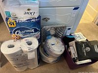 Photo showing Charmin Ultra Soft toilet paper, Dove Sensitive Skin facial tissues, disposable plates, aluminum foil trays, and boxed beauty and first aid items in plastic storage tubs.