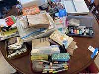 Photo of assorted scrapbook supplies on a table including paper cutter, pens, ribbons, and boxed embellishments.