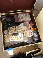 Overhead photo showing an open storage container filled with multiple bags and containers of scrapbook supplies including buttons, embellishments, stickers, velcro strips, and googly eyes.