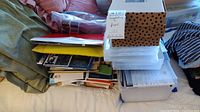 Photo showing large assortment of scrapbooking materials stacked with plastic folders and albums on top of bed