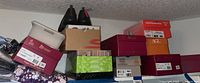 Multiple shoe boxes stacked together, some open revealing shoes and scrapbooking items inside