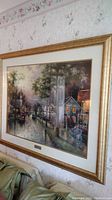 Framed print mounted on floral wallpaper above a sofa, showing street scene artwork with reflections on glass.