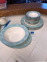 Stack of plates, soup bowls, and saucers showing blue leaf pattern on cream background with gold trim
