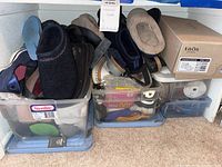 Shelf with multiple women's shoes and slippers in black, brown, and navy, packed in plastic Sterilite bins and boxes.