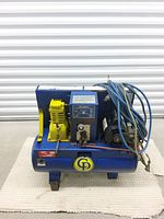 Blue GD brand air compressor with attached electric motor, yellow pump, pressure gauge, and coiled blue hose.