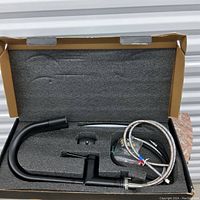 Photo of the matte black kitchen faucet with hoses and installation parts inside protective foam packaging.