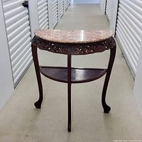 Front view of a semi-circular entry table with brown granite top and dark wood carved legs in a hallway.