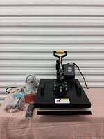 Photo of black heat press machine with control panel, rotary handle, and accompanying accessories.