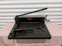 Full view of heavy duty paper cutter showing base with red measurement grid, handle, and clamp mechanism