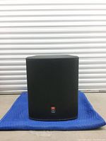 Front view of JBL PRX718S subwoofer on moving blanket in front of roll-up door