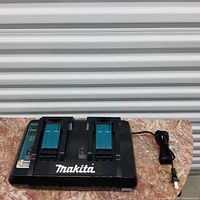 Front view of Makita dual battery charger showing slots for two batteries, Makita logo in white, and attached power cord.