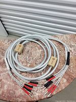 Two coiled silver braided speaker cables lying on marble surface, showing wooden spacers and multiple banana plug ends