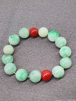 Complete view of the bracelet showing round apple green jade beads and two red beads.
