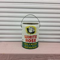 Front view of a vintage White Rose motor oil tin featuring a white rose logo, brand name, and heavy duty markings, with a metal wire handle on top.