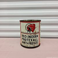 Front view of a cylindrical metal tin labeled 'Red Indian Protexall Antifreeze' with a red Native American head logo, showing aging and wear.
