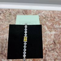 Full view of silver tennis bracelet on display backing showing overall design with clear and yellow stones.